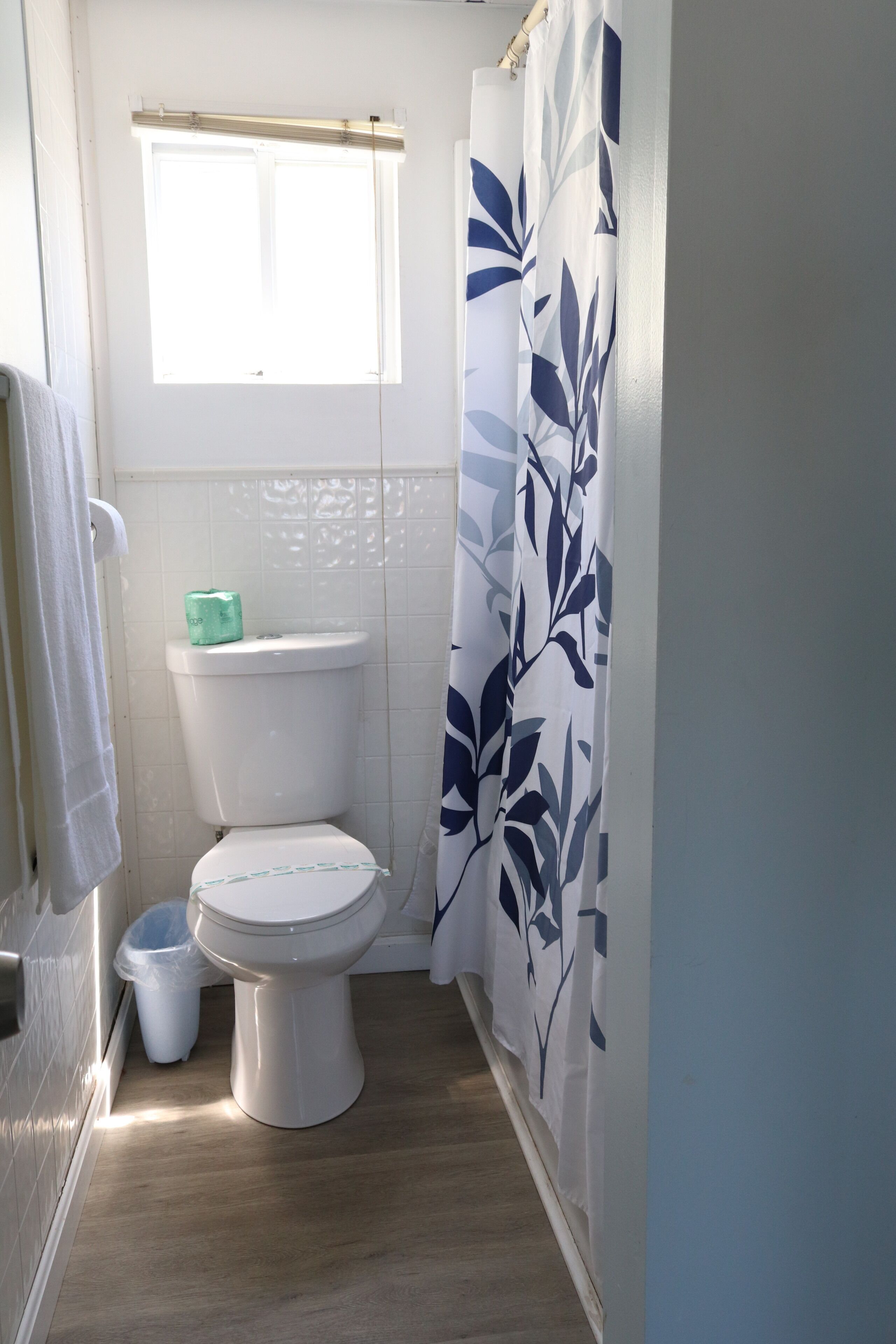 A small, clean bathroom with a toilet, a trash bin, and a shower curtain with a leaf pattern.