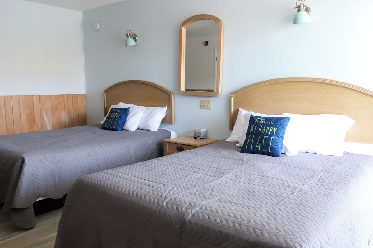 Two twin beds with headboards, a bedside table with a lamp, a wall-mounted mirror, and a small shelf with decorative items.