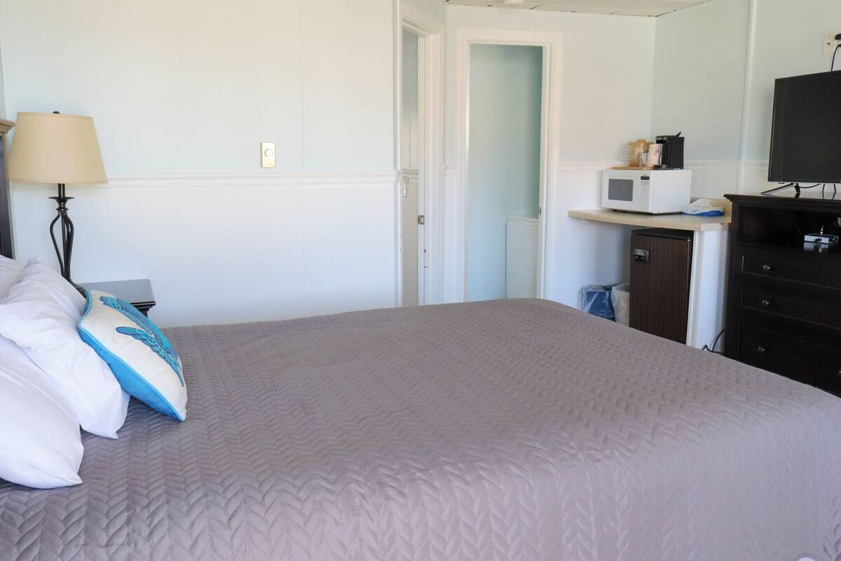 A hotel room with a bed, a lamp, a microwave, a TV, and a small cabinet.