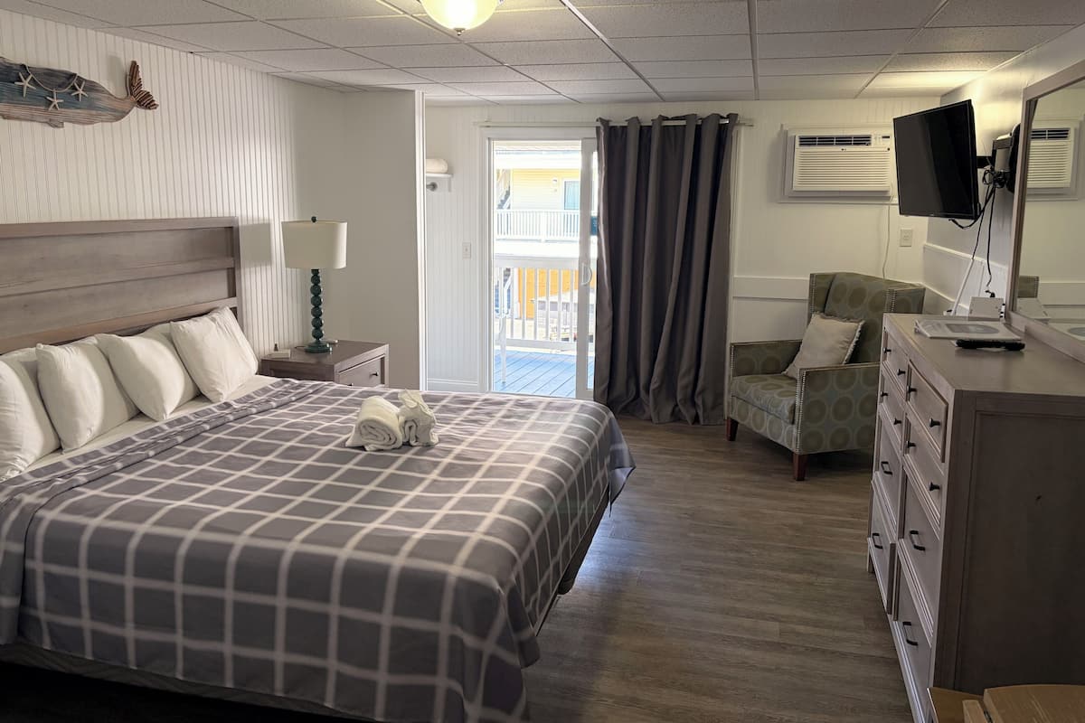A hotel room with a bed, a chair, a dresser, a television, and a view of the outside.