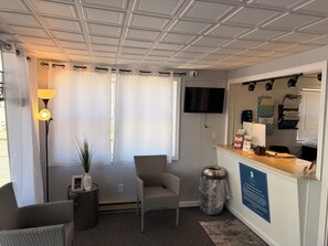 A hotel room with a flat-screen TV, a desk with a computer, a chair, a lamp, and a trash can. - Mainsail Inn & Cottages (Hampton)