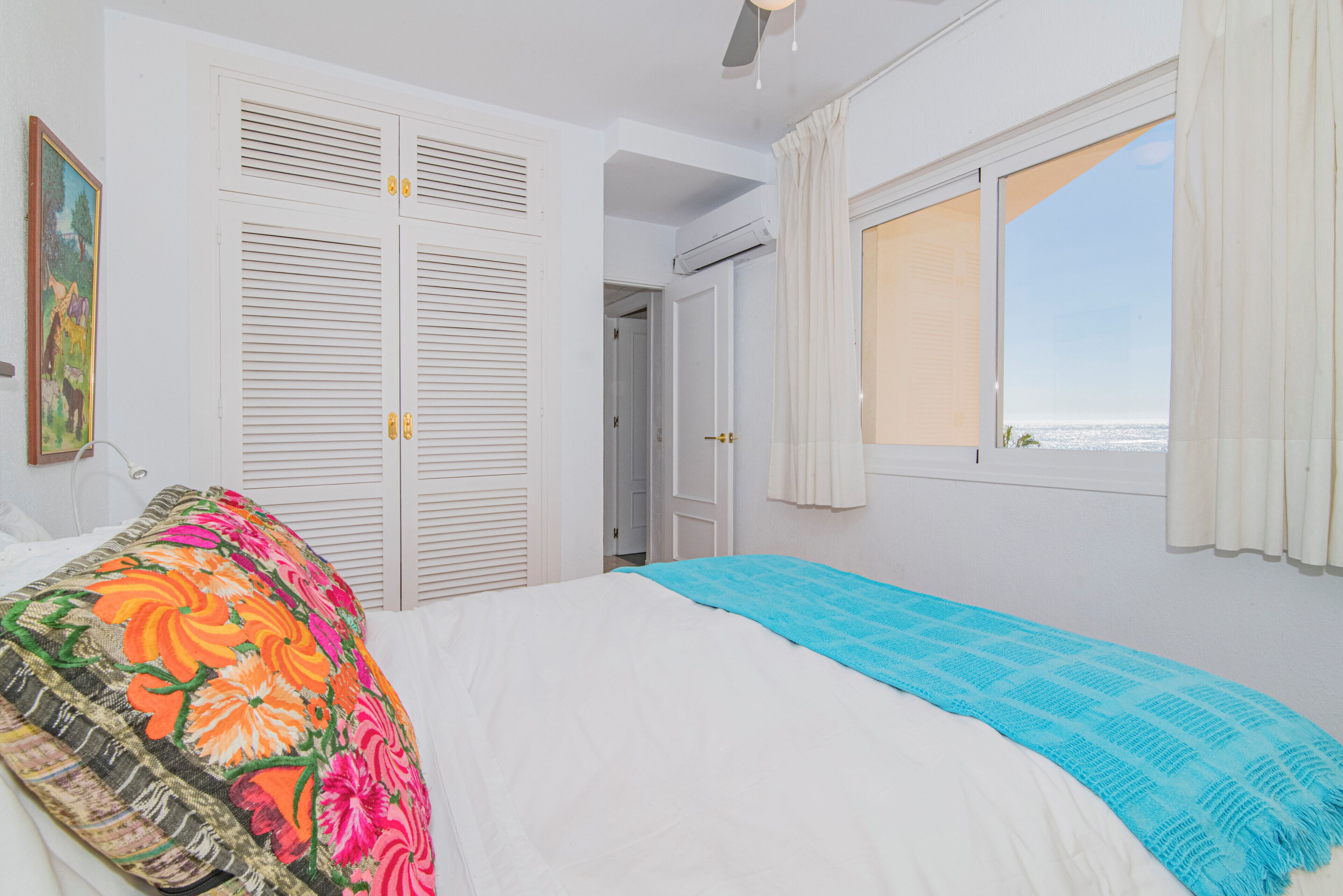 A bedroom with a bed, a window with curtains, a door, and a painting on the wall.