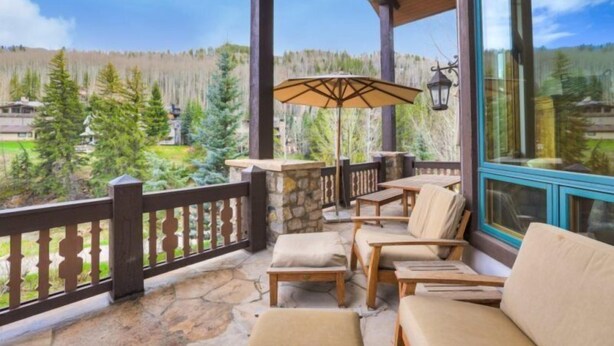 A covered outdoor seating area with stone flooring, wooden furniture, and a view of a forested landscape. - 5 Bedroom Luxury Townhome in Lionshead Village (Vail)