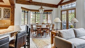 A spacious dining area with a round table and chairs, large windows with a view of greenery, and a rustic wooden ceiling. - 5 Bedroom Luxury Townhome in Lionshead Village (Vail)
