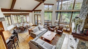 A spacious living room with a wooden floor, large windows, and a stone fireplace. - 5 Bedroom Luxury Townhome in Lionshead Village (Vail)