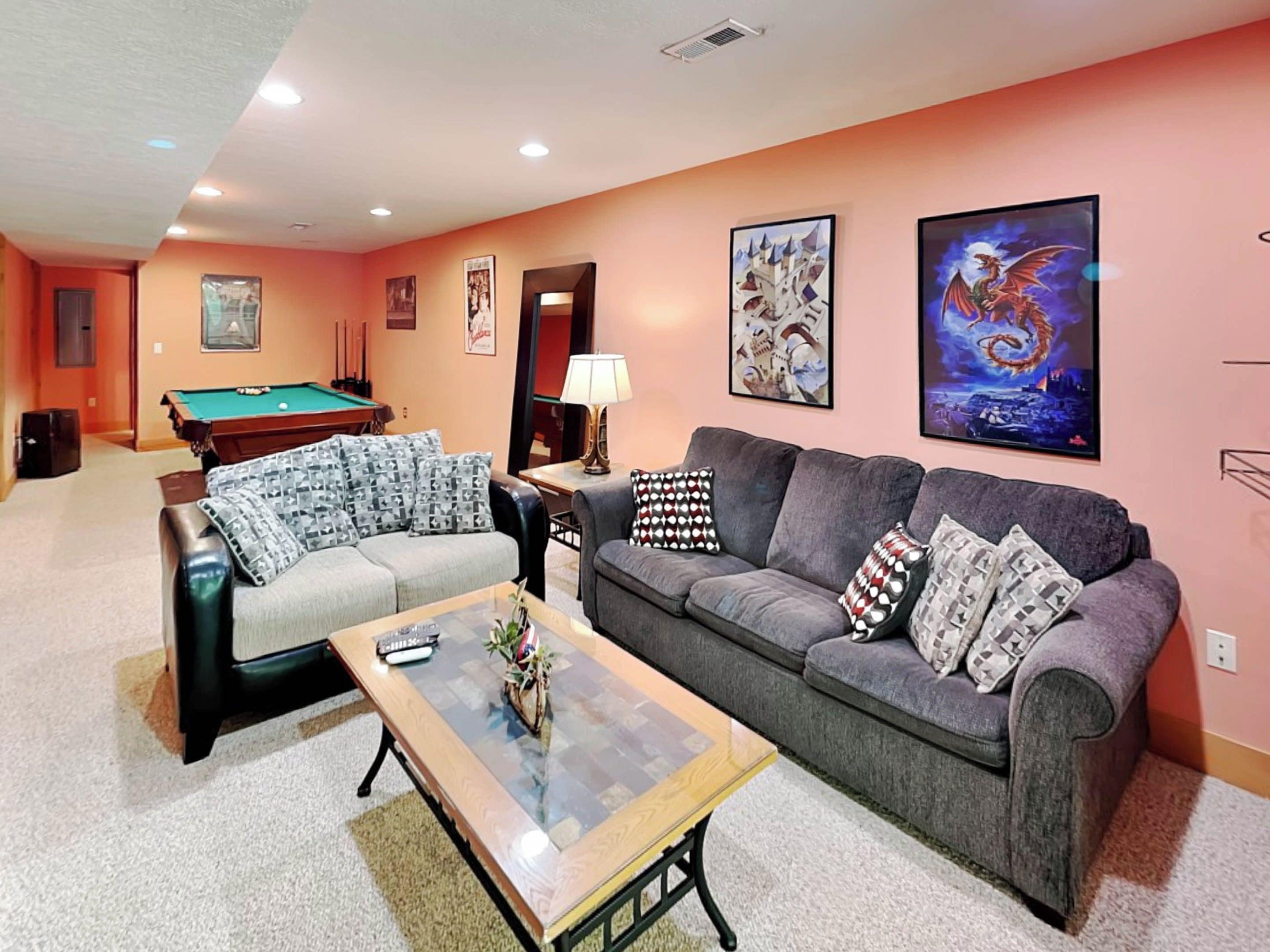 A living room with a pool table, two sofas, a coffee table, and artwork on the walls.