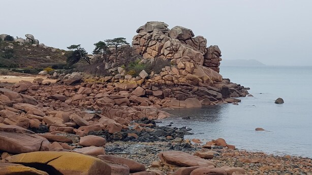 Eine felsige Küstenlinie mit großen Felsen und ruhiger See.