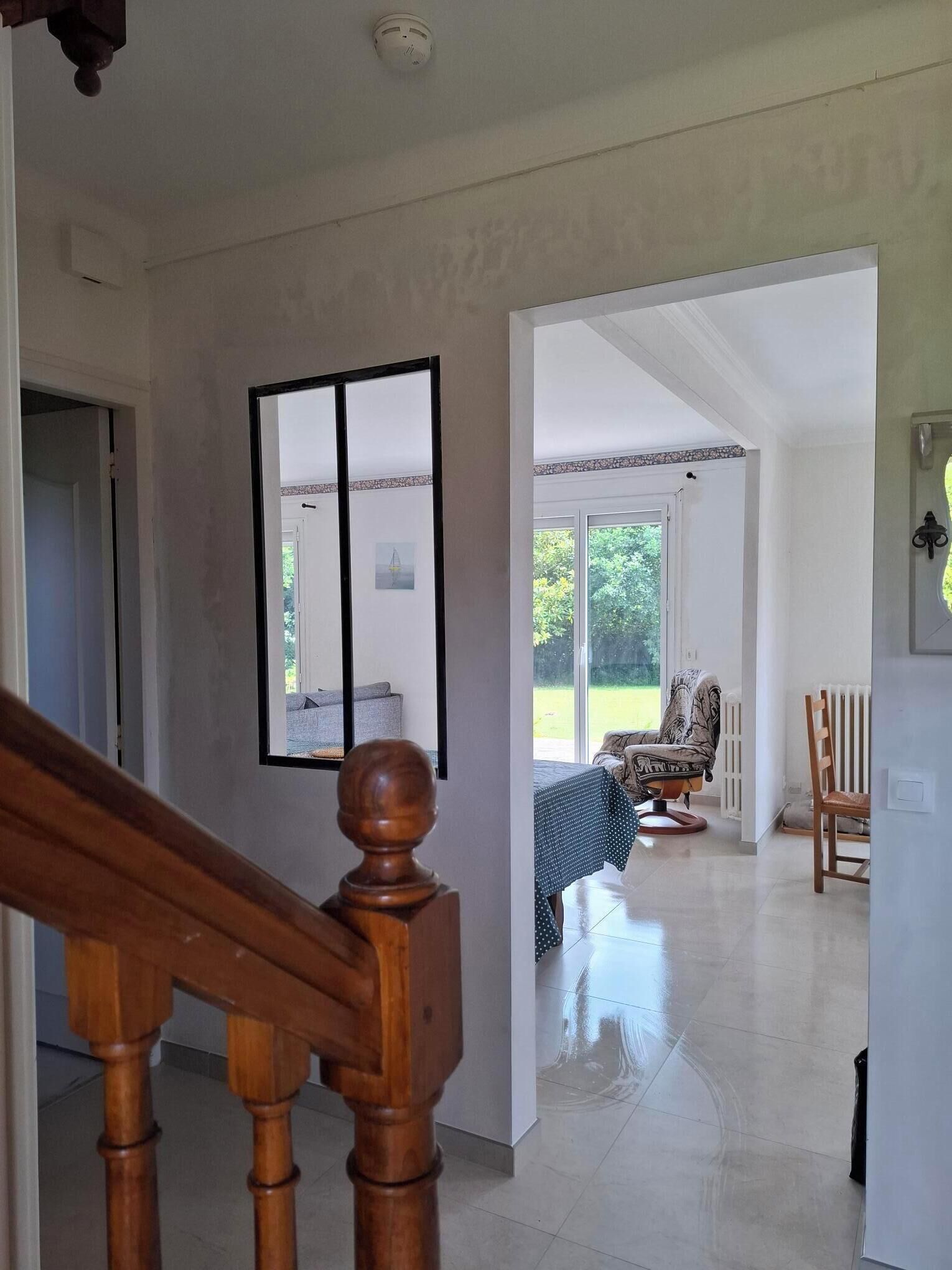 Un vaste espace de vie doté d’un haut plafond, d’un escalier en bois et d’une grande fenêtre offrant une vue sur l’extérieur.