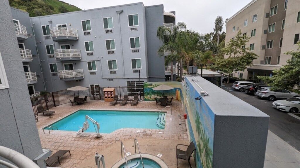 A pool area with a rectangular pool, lounge chairs, and a small deck.