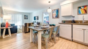 Une cuisine moderne avec des meubles blancs, un coin repas avec une table et des chaises en bois, et un salon avec un canapé et une lampe.