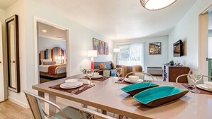 A modern hotel room with a dining area, a living room, and a bedroom.
