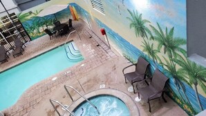 Zwembadgedeelte met een muurschildering van palmbomen en een strandscène, omringd door ligbedden en een jacuzzi.