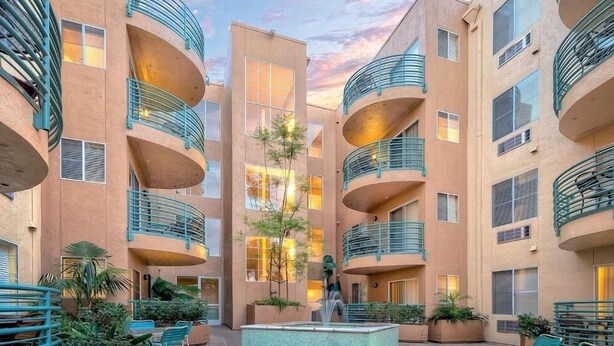 A multi-story residential building with balconies, a central courtyard with seating and a fountain, and a sunset sky. - WorldMark Mission Valley - 1 Bedroom (San Diego)