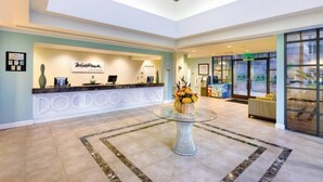 A hotel lobby with a reception desk, a glass-top table with flowers, and a large window. - WorldMark Mission Valley - 1 Bedroom (San Diego)