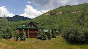 A lodge with a green roof and multiple windows, surrounded by lush greenery and mountains. - Wilderness Cabin In Colorado Mountains (Gunnison County)