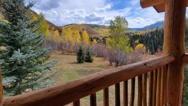 A wooden deck with a view of a forested valley and hills. - Wilderness Cabin In Colorado Mountains (Gunnison County)