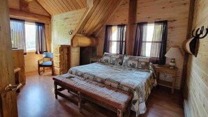 A wooden cabin bedroom with a bed, bench, chair, and a small table with a lamp. - Wilderness Cabin In Colorado Mountains (Gunnison County)
