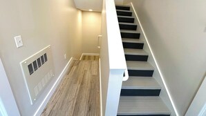 Eine moderne Treppe mit hellem Holzboden und dunklen Stufen, die zu einer Zwischenebene mit Geländer führt.
