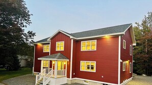 Ein zweistöckiges Haus mit roter Fassade, einer Veranda mit Treppe und mehreren erleuchteten Fenstern.