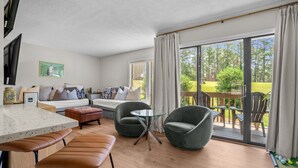 Un salon moderne comprenant un canapé, deux fauteuils, une table basse en verre et un coin repas avec un tabouret de bar.