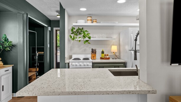 Une cuisine moderne dotée d’un plan de travail en granit, de meubles blancs et d’une cuisinière intégrée.