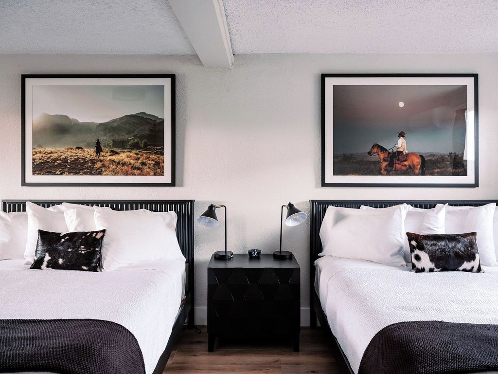 A hotel room with two beds, a nightstand with lamps, and two framed pictures on the wall.