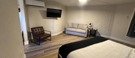 Une chambre à coucher comprenant un lit, un canapé, une chaise, un téléviseur et un appareil de climatisation.