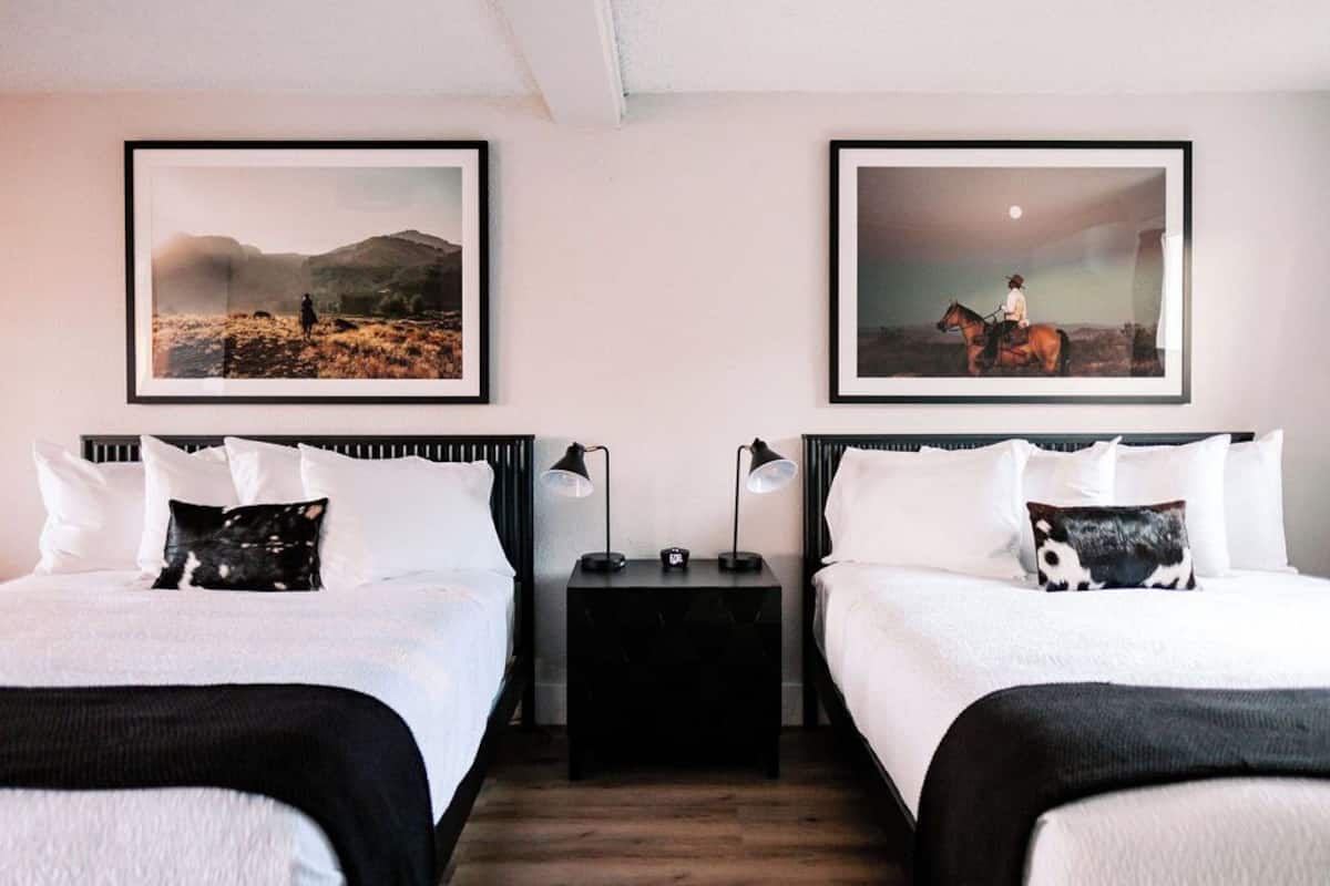 A hotel room with two beds, white bedding, black headboards, and two nightstands with lamps.