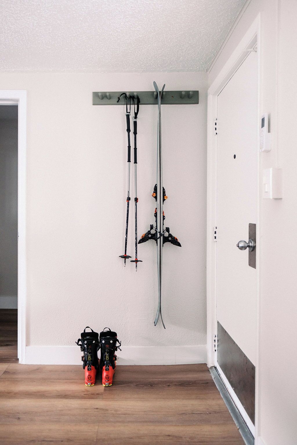 A room with a ski rack mounted on the wall and a pair of skis and ski boots on the floor.