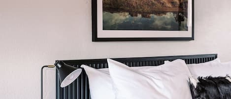 Un dormitorio con cama, mesita de noche, un cuadro enmarcado y una lámpara.