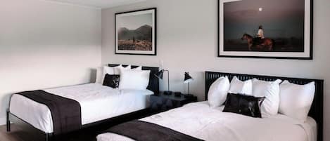 A hotel room with two beds, each with white bedding and black headboards. There are two framed pictures on the wall, one depicting a desert landscape and the other a person on horseback.