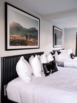 Una habitación de hotel con una cama grande, cabecera y un cuadro enmarcado de un paisaje.