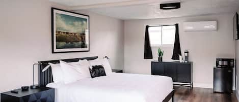 A modern bedroom with a large bed, a nightstand, a dresser, and a window with curtains.