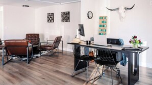 Un salon moderne avec un plancher en bois, des fauteuils en cuir, un bureau en métal noir et une horloge murale.