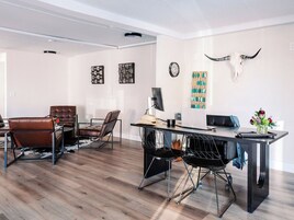 Una sala de estar moderna con piso de madera, sillones de cuero, un escritorio de metal negro y un reloj fijado a la pared.