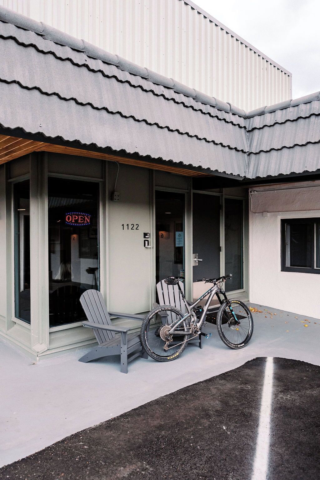 A building with a corrugated metal roof, a bicycle parked outside, and a chair near the entrance.