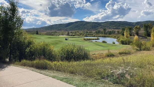 Un parcours de golf avec un étang, des arbres et des collines en arrière-plan.
