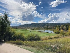 Un campo de golf con un estanque, árboles y colinas al fondo.