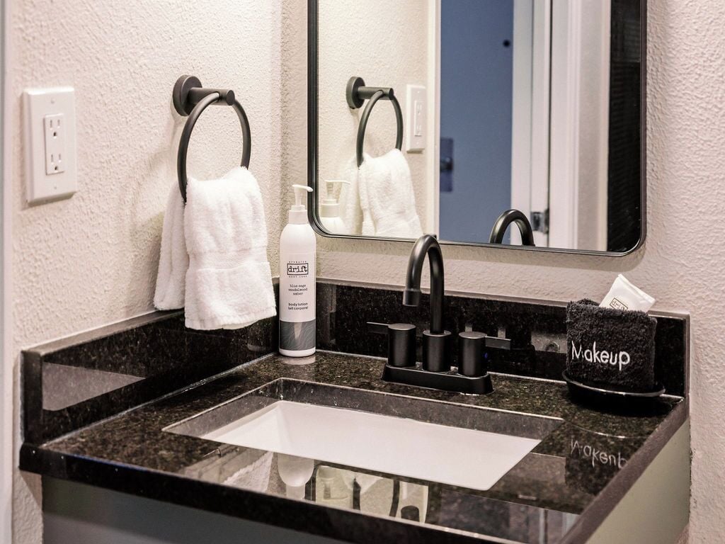 Une salle de bain avec un lavabo en granit noir, un miroir, un porte-serviettes, un flacon de lotion pour le corps et une trousse de maquillage.