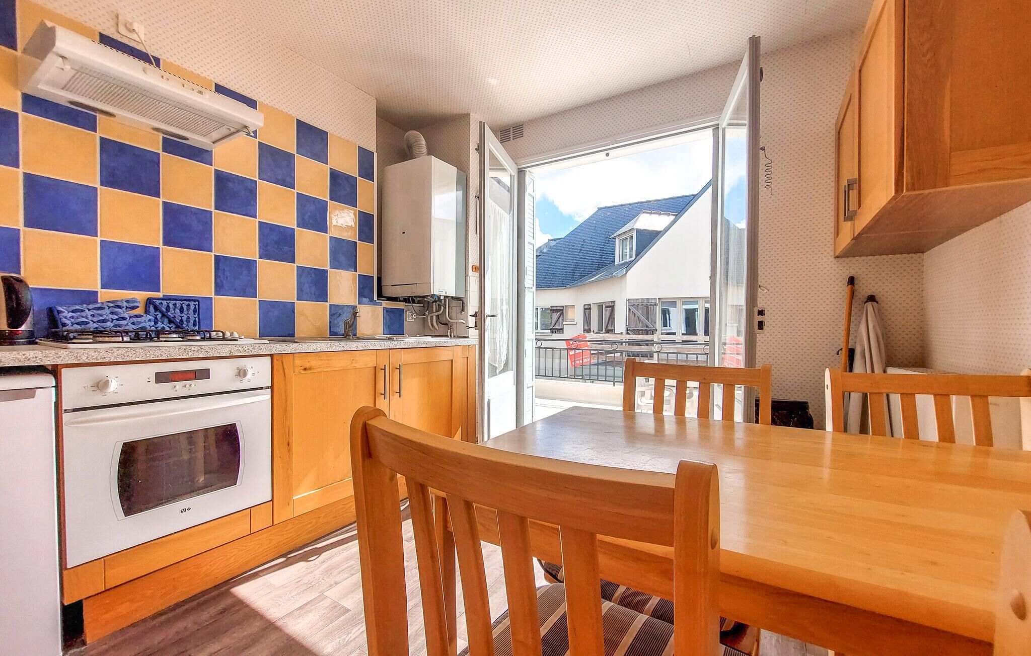 A kitchen with a checkered backsplash, wooden cabinets, a stove, and a dining area with a table and chairs.