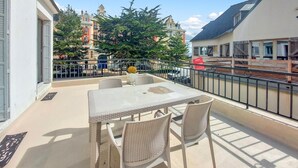 Ein Balkon mit Tisch und Stühlen, einem Metallgeländer und Blick auf Gebäude und Bäume.