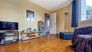 Ein Wohnzimmer mit Fernseher, Bücherregal und einem großen Fenster mit Vorhängen.