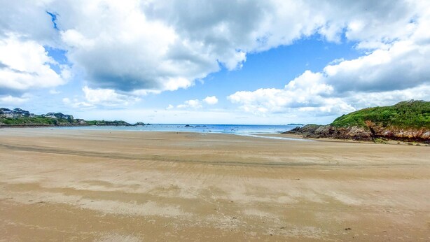 Ein weiter Sandstrand mit blauem Himmel und vereinzelten Wolken.