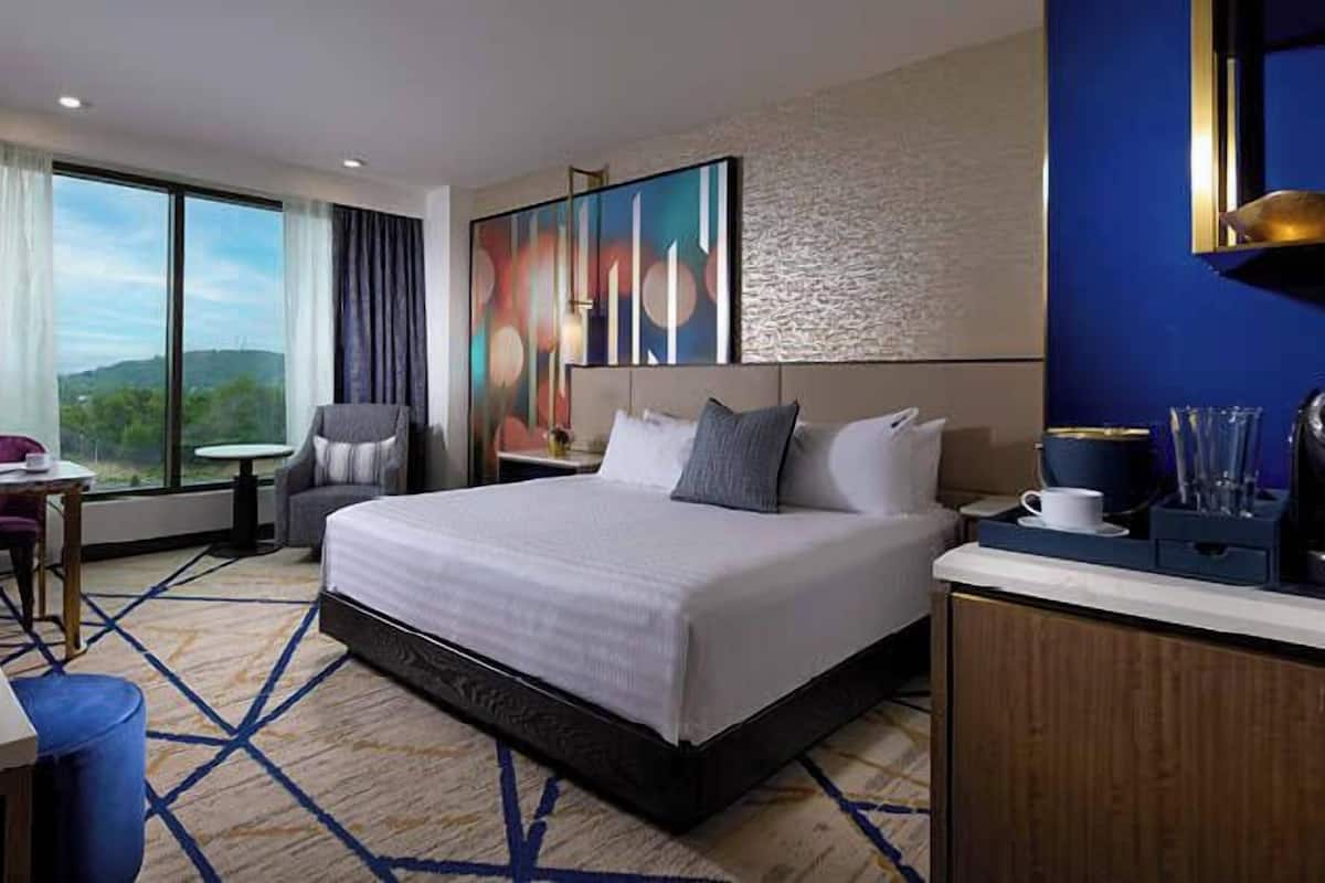 Une chambre d’hôtel avec un grand lit, un bureau avec un ordinateur portable, une chaise, une machine à café et une vue sur l’extérieur.