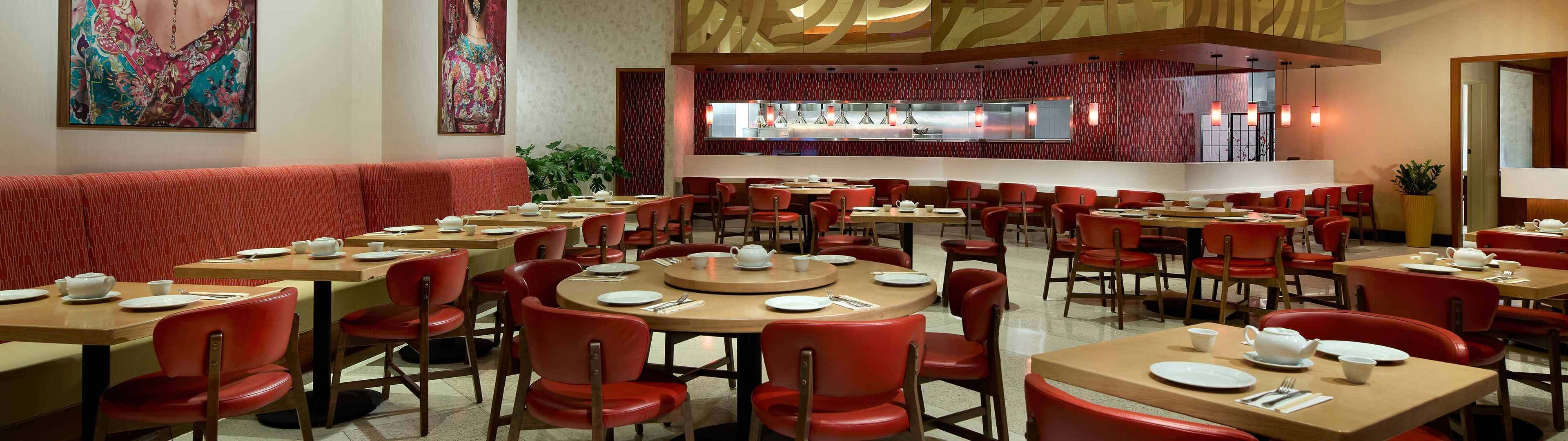 A restaurant with multiple tables and red chairs, a bar area, and decorative wall art.