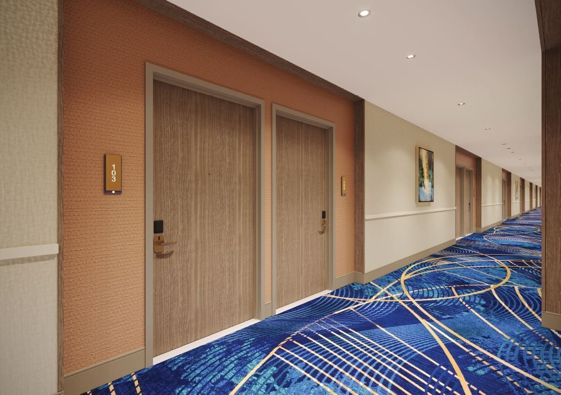 A hotel corridor with wooden doors, a carpeted floor, and a number sign on the wall.
