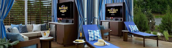 Habitación del Hard Rock Hotel & Casino con sofá, sillones, una pequeña mesa con una bebida y un televisor sobre un mueble bajo.