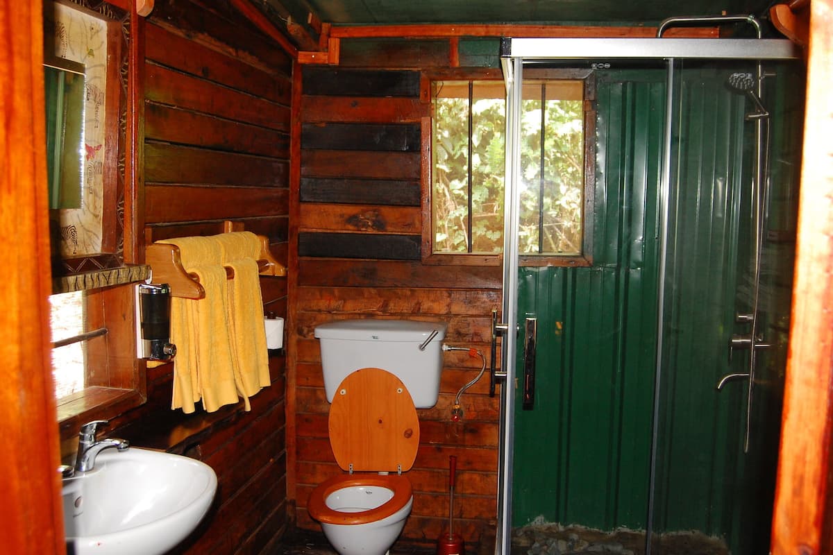 A wooden cabin bathroom with a toilet, sink, and shower.