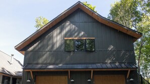 Une maison à deux étages, à l’extérieur sombre, avec un grand garage et un porche à l’avant, agrémenté de plantes en pot.