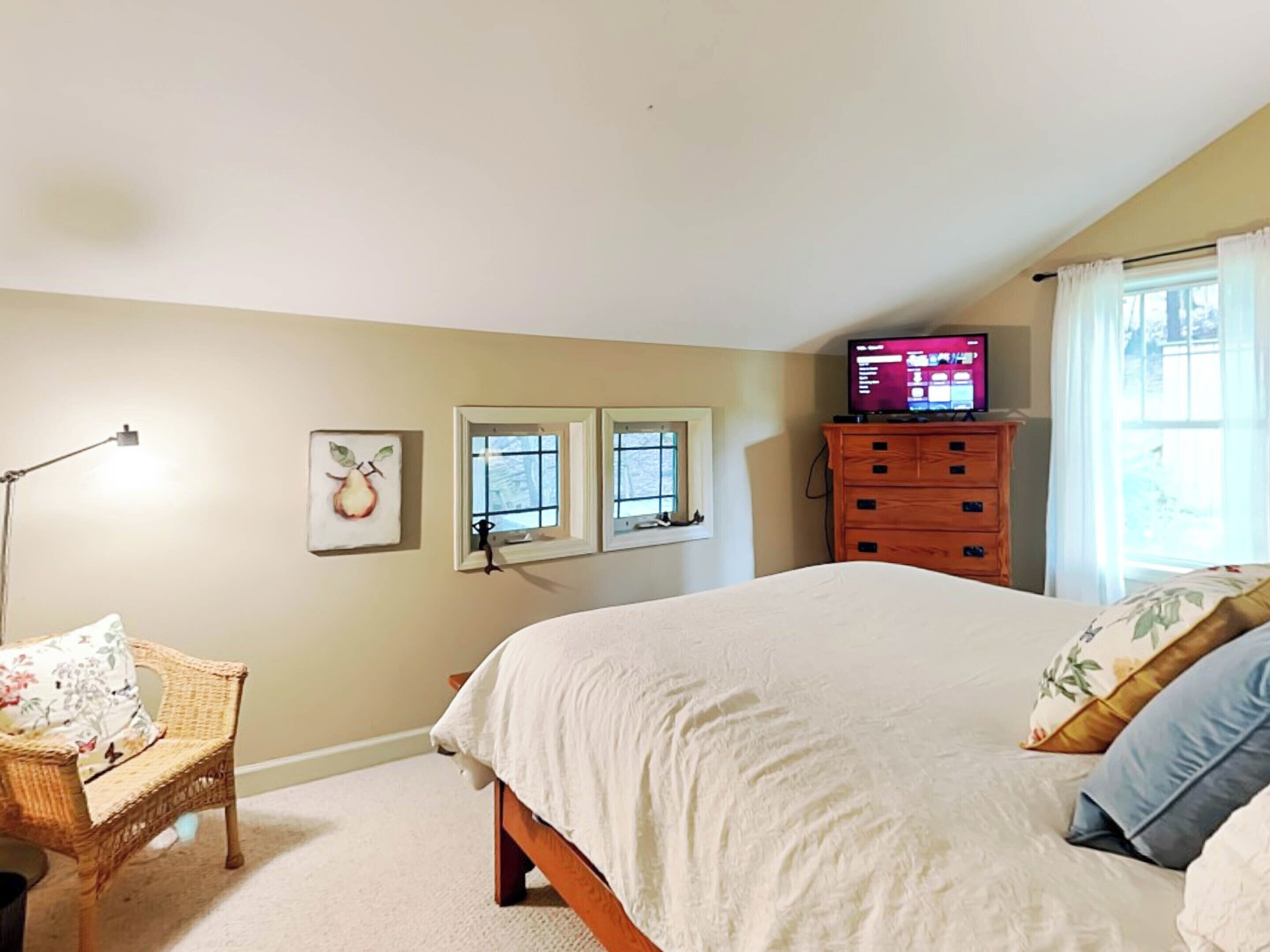 A bedroom with a large bed, a dresser, a chair, and a television on a dresser.